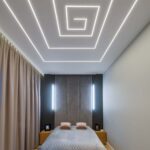 LED pásky zapuštěné ve stropě ložnice s manželskou postelí vytvářející optický klam